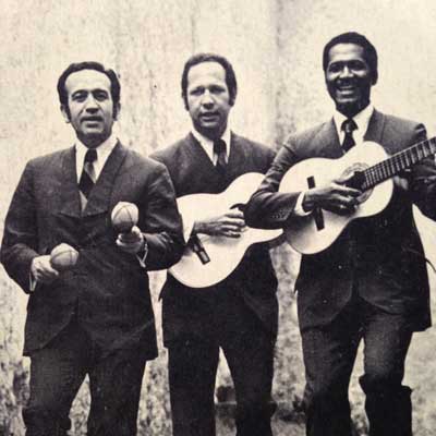 Los tres integrantes del Trío Los Isleños posando juntos en una noche tropical.